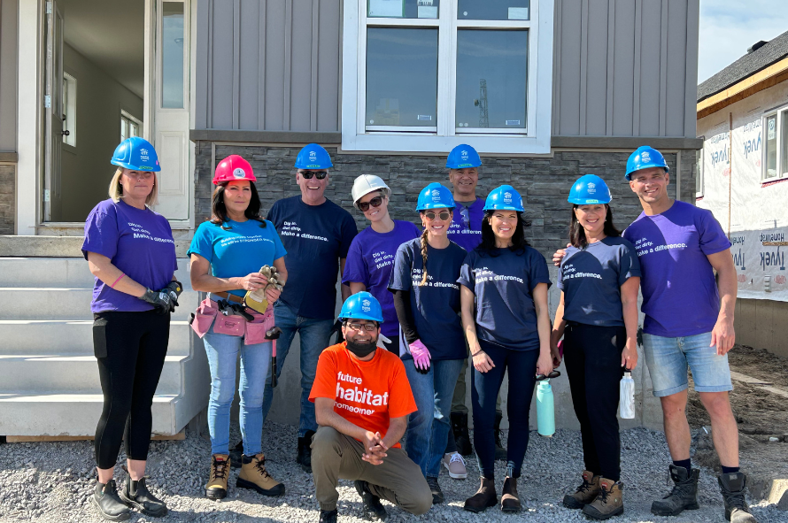 L'équipe McGarr Realty d'Habitat pour l'humanité porte des chemises, des casques et des bottes à embout d'acier de bénévoles, souriant devant une maison partiellement construite