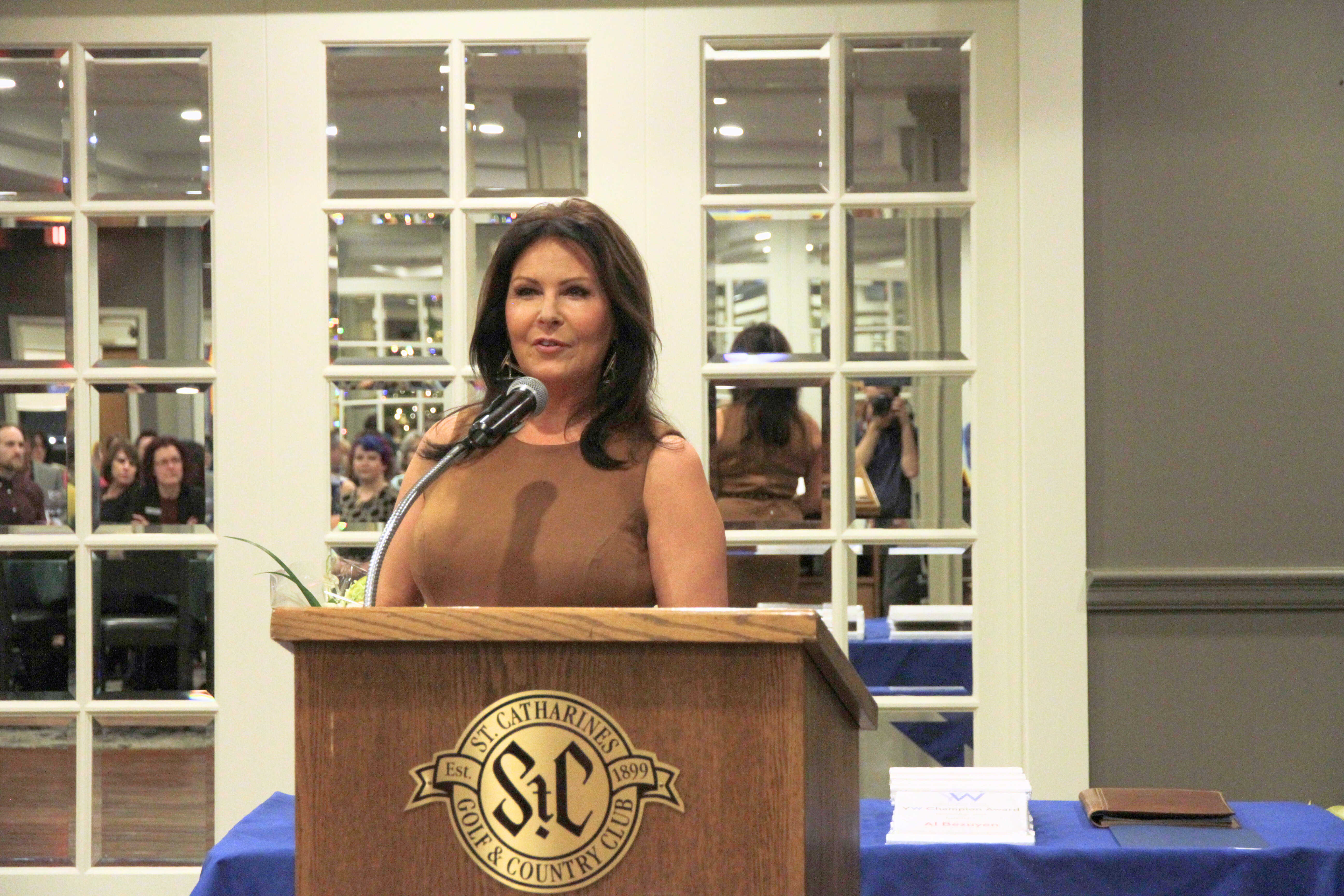 Cindi stands at a podium in front of a group of seated attendees at a YWCA AGM