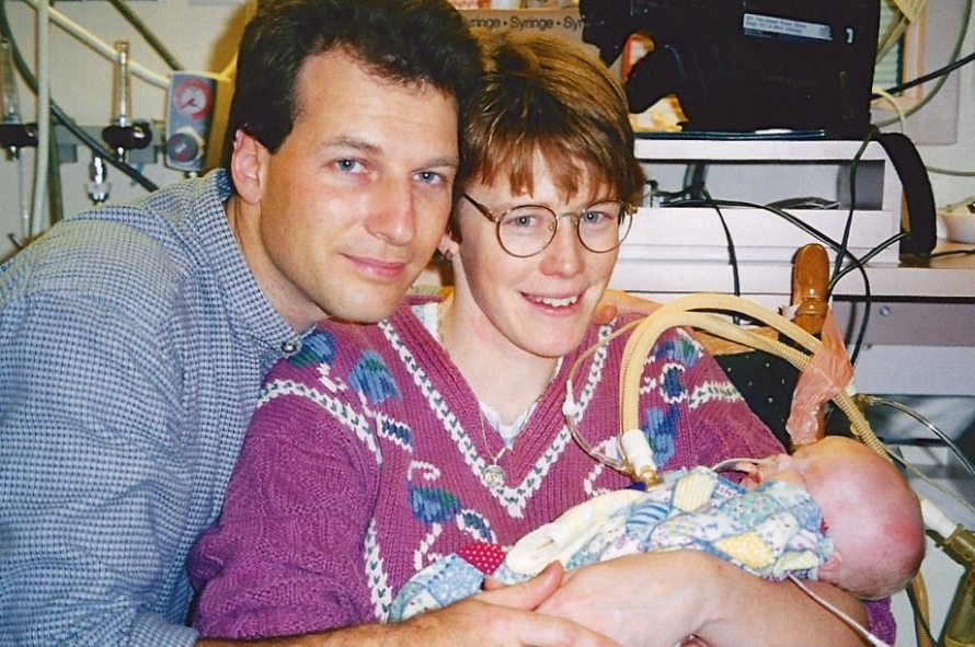 Bruce and Mary holding Alyssa who is hooked up to breathing machines and monitors -- Bruce et Mary tiennent Alyssa qui est connectée à des appareils respiratoires et à des moniteurs